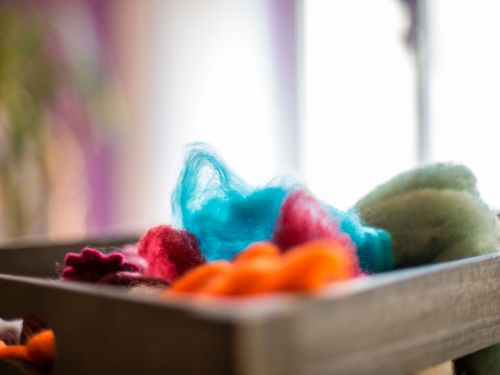 Detailansicht mit selektiver Schärfe auf eine Holzkiste mit Filzgegenständen, im Hintergrund unscharf der Raum/Fenster