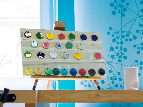 Buntglasierte runde Tonscheiben hängen auf einem Präsentationskarton auf einer Tischstaffelei