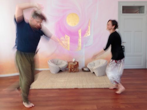 Therapeutin und Patient tanzen weit auseinander vor bemalter Wand in Rosa- und Violetttönen, Bewegungsunschärfe