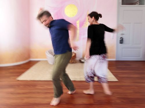 Therapeutin und Patient tanzen seitlich zueinander vor bemalter Wand in Rosa- und Violetttönen, fotografiert mit Bewegungsunschärfe