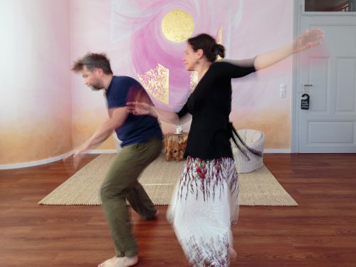 Therapeutin und Patient tanzen frei im Raum 1 vor bemalter Wand in Rosa- und Violetttönen, fotografiert mit Bewegungsunschärfe